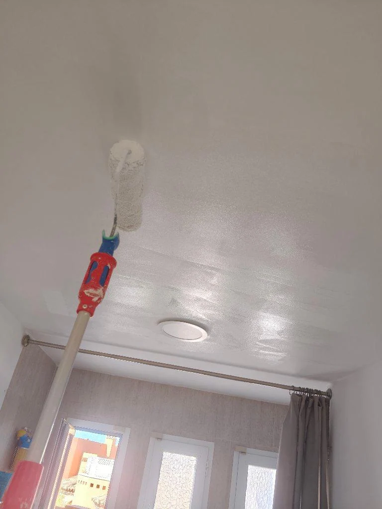 Aplicación de pintura con rodillo en un techo junto a una ventana