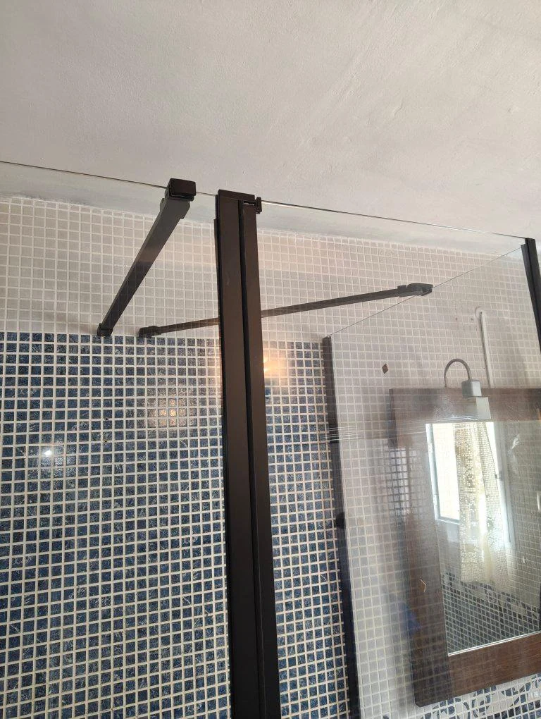 Detalle superior de una mampara de perfiles negros instalada en un baño